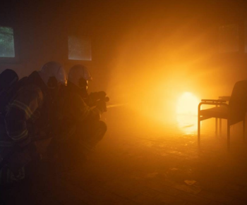 Two people dressed in firefighting gear practising a drill to fight a fire.