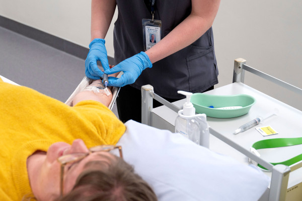 A patient is lying down as a health worker gives them an isotope injection. This is where a small amount of radioactive material (tracer) is injected into the body to help visualise organs, tissues, or bones using nuclear medicine imaging.