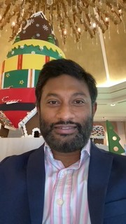 Pradeep Kumar wearing a shirt with blue, pink and grey stripes and a navy jacket.