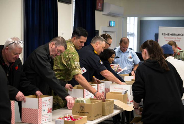 people gather to pack boxes with treats for soldiers stationed overseas. There are representatives from all the Defence Forces, school kids and the wider community packing.