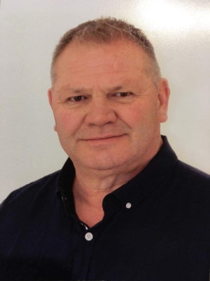 This is a portrait photo of Mark Brown, Procurement Lead for the SPCA. He is shown looking directly at the camera. He has tight cropped dark blonde hair. He has dark brown eyes. And he is wearing a black shirt.