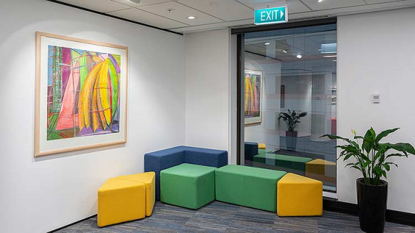 An example of contemporary design, showing a number of multi-coloured soft furnishings with a plant and a piece of abstract art on the wall.