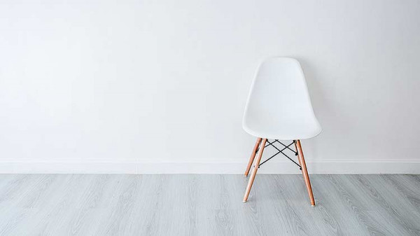 An example of low visual contrast, showing a white chair on a white wall with a grey floor.